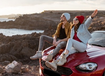 Couple sitting on hood of red convertible on mountain near the ocean