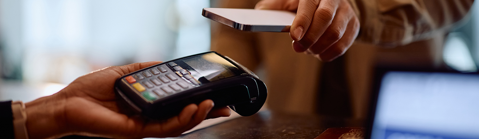 Close-up photo of a customer using a smartphone to make a contactless payment on a handheld credit card terminal.